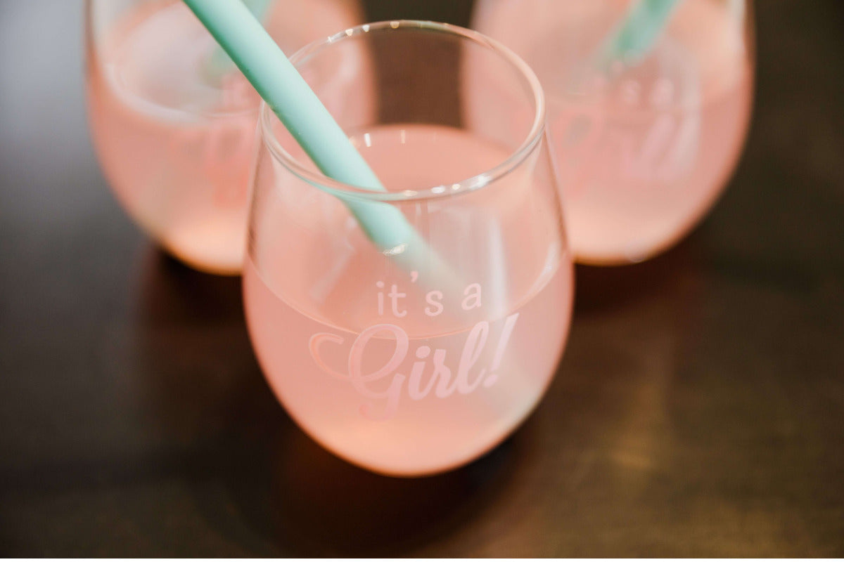 Close-up of three glasses with pink lemonade and mint green straws, each etched with "It's a Girl" in frosted white lettering — perfect for a Sip and See party celebration.
