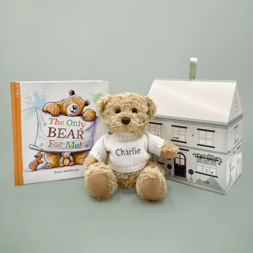 Tan plush teddy bear in a white embroidered knit sweater with the name "Charlie" beside "The Only Bear For Me!" hardcover picture book and a house-shaped illustrated gift box — personalized sibling bear and book gift set.
