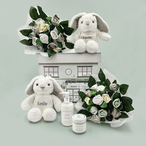 Two grey plush bunnies, reversible hats, scratch mittens, socks, and natural baby skincare in a gift box — luxury personalized twins baby gift set for two newborns.