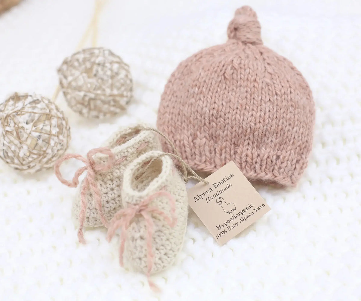 Handmade blush pink baby alpaca knotted cap and bootie set, flat lay, newborn size, soft natural fiber