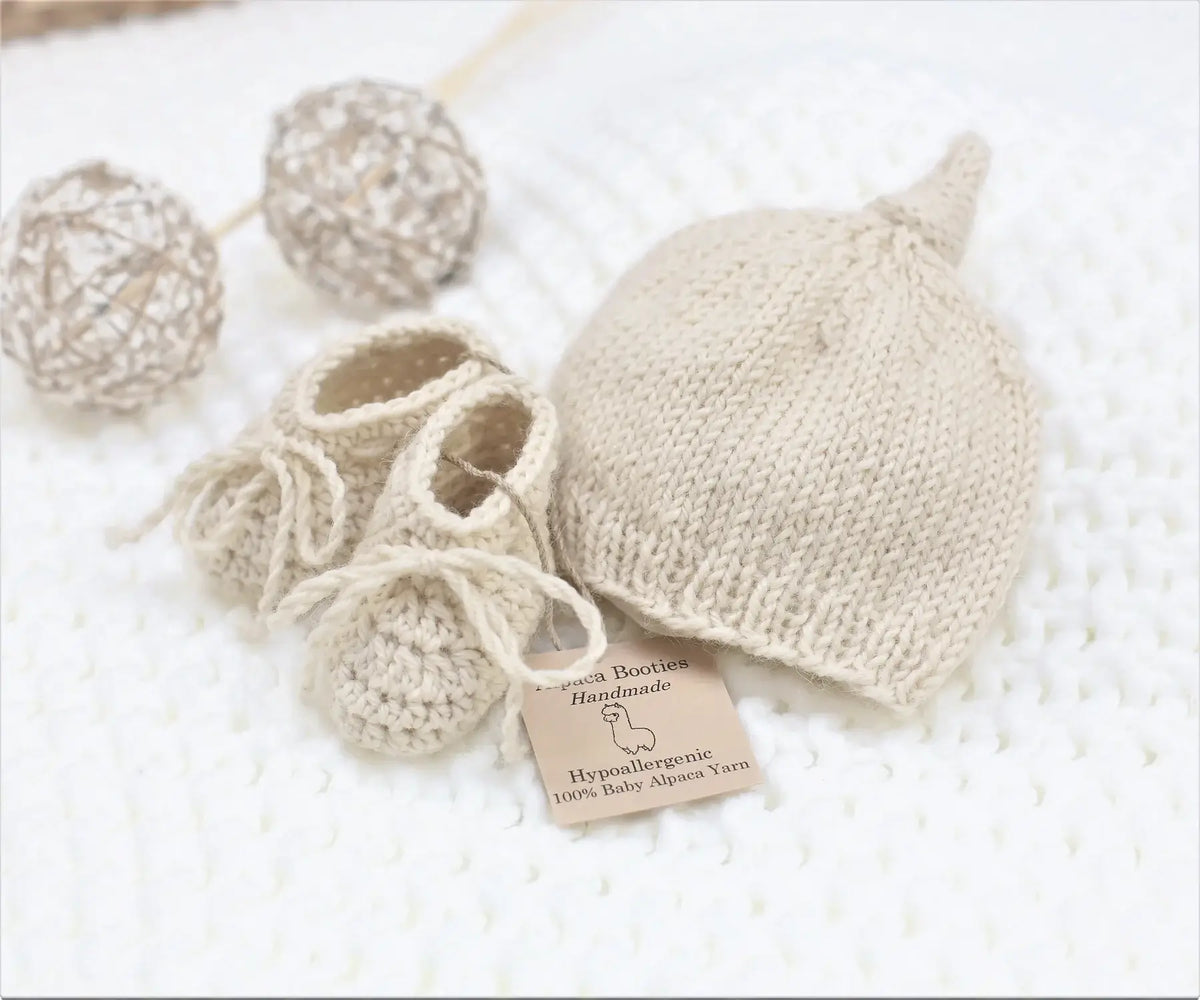 Handmade natural baby alpaca knotted cap and bootie set, flat lay, newborn size, gender neutral