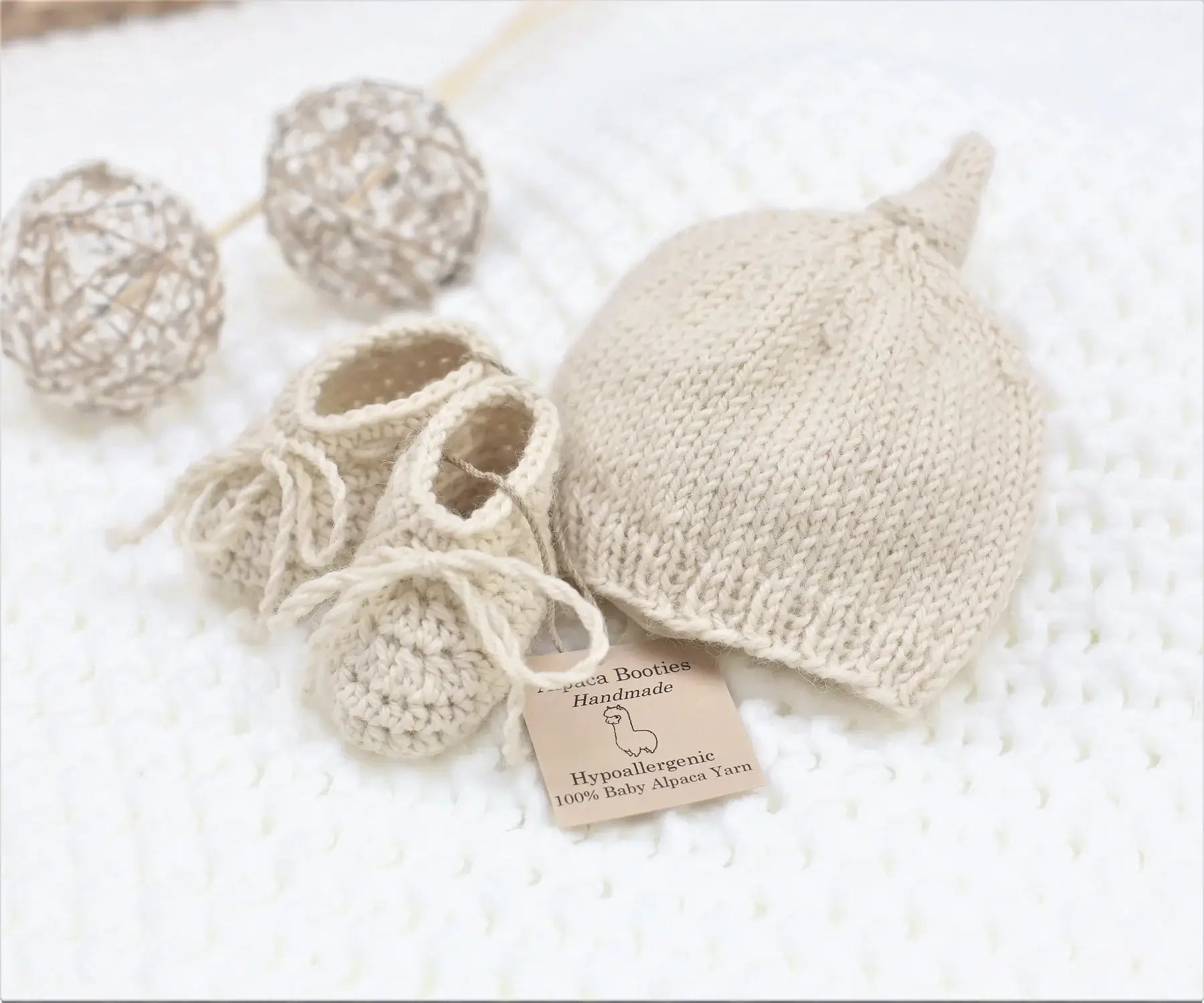 Handmade natural baby alpaca knotted cap and bootie set, flat lay, newborn size, gender neutral
