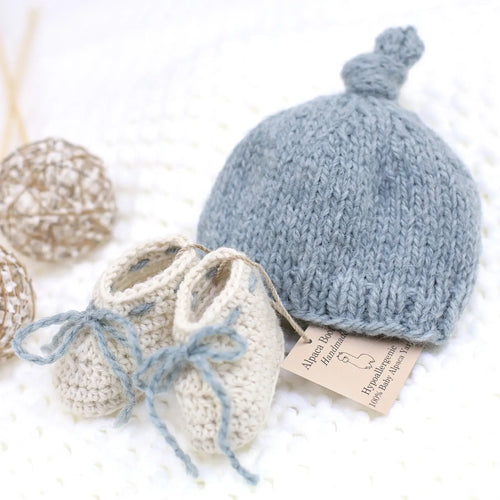 Handmade sky blue baby alpaca knotted cap and bootie set, flat lay, newborn size, soft natural fiber