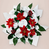 Close-up of white baby clothes rolled into roses with red poinsettias and holly berries