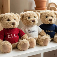 Close-up of three Christmas teddy bears in red, navy, and white knitted sweaters sitting on a shelf