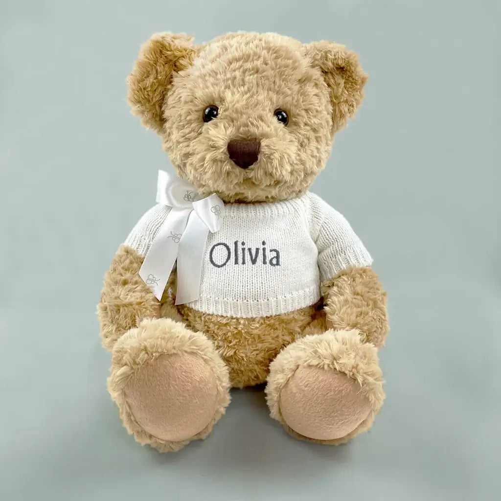 Personalized baby teddy bear keepsake gift in white knit sweater with embroidered name and white ribbon bow — neutral gray